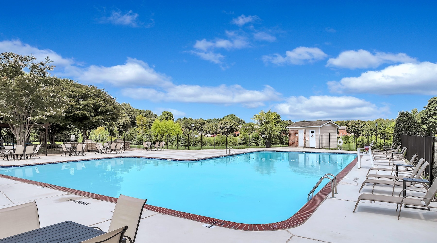 resort style pool with seating with a trees behind it